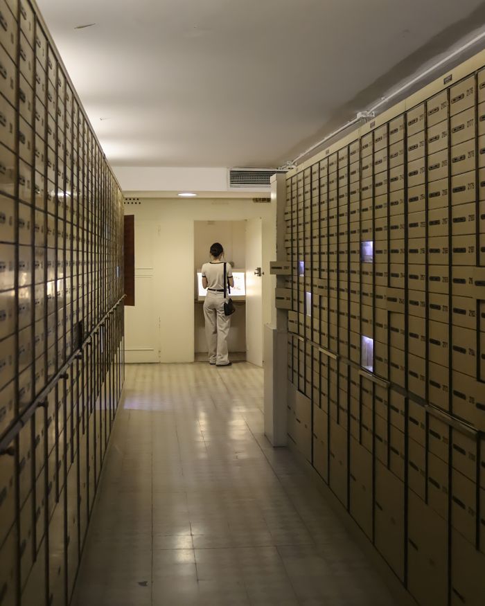A woman examines a locker inside a secure vault lined with metal safety deposit boxes.